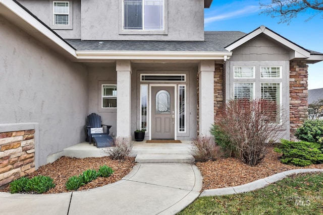 entrance to property featuring stone siding, stucco siding, and roof with shingles