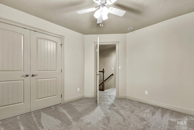 unfurnished bedroom featuring a textured ceiling, a closet, carpet floors, baseboards, and ceiling fan