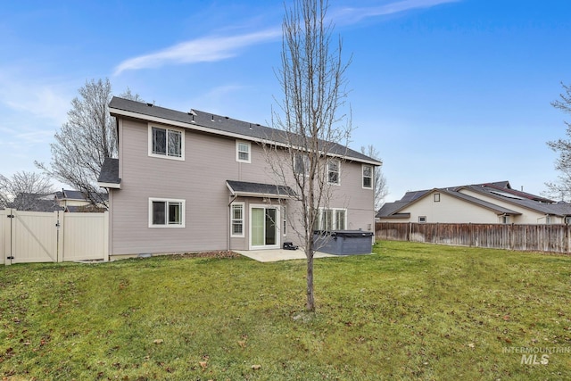 rear view of property featuring a gate, a fenced backyard, a hot tub, a patio area, and a lawn