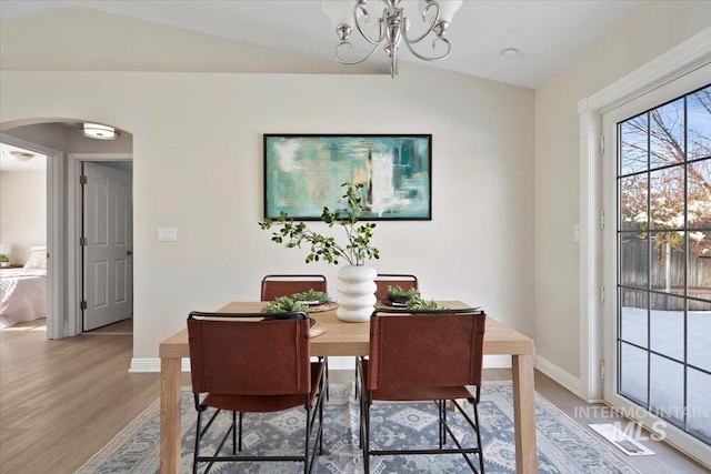 dining space with lofted ceiling, wood-type flooring, and a chandelier