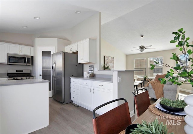 kitchen with vaulted ceiling, light wood-type flooring, ceiling fan, stainless steel appliances, and white cabinets