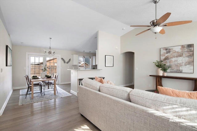 living room with dark wood-type flooring, ceiling fan with notable chandelier, and high vaulted ceiling