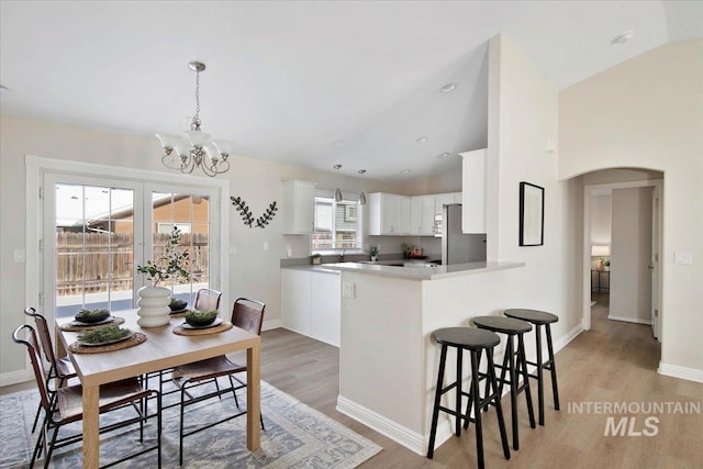 kitchen with pendant lighting, stainless steel fridge, white cabinets, kitchen peninsula, and light wood-type flooring