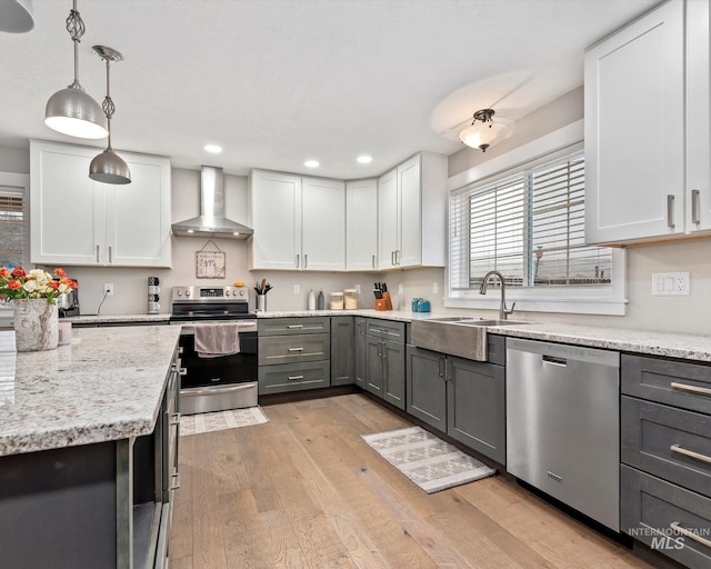 kitchen with gray cabinetry, stainless steel appliances, hanging light fixtures, white cabinetry, and wall chimney range hood