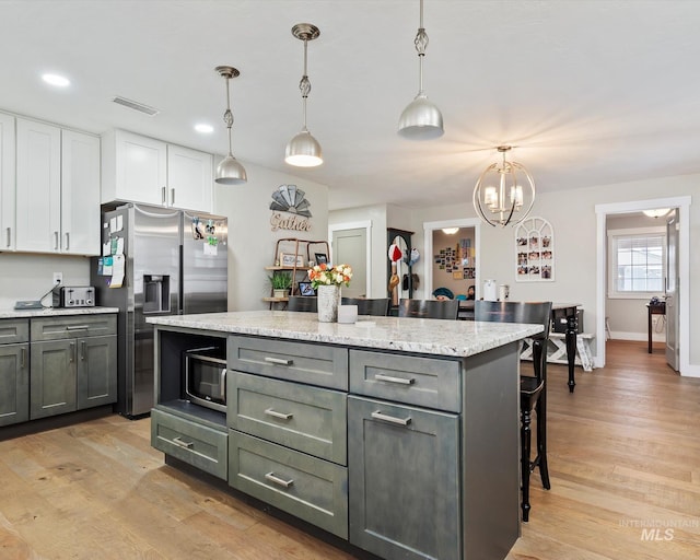 kitchen featuring pendant lighting, a center island, stainless steel appliances, light hardwood / wood-style floors, and white cabinets