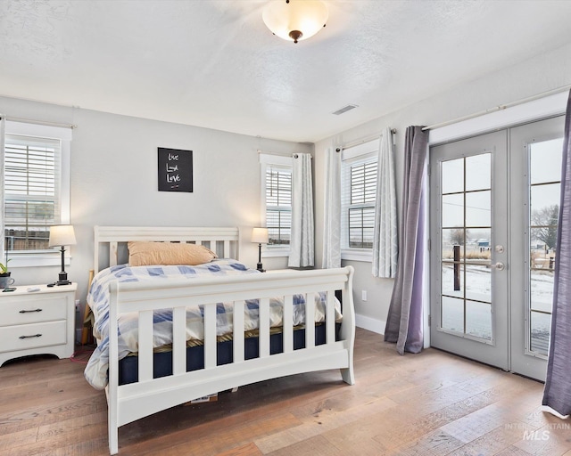 bedroom featuring french doors, a textured ceiling, access to outside, and light hardwood / wood-style floors