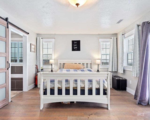 bedroom featuring a textured ceiling, multiple windows, light hardwood / wood-style floors, and a barn door