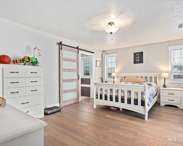 bedroom with a textured ceiling, a barn door, and light hardwood / wood-style flooring