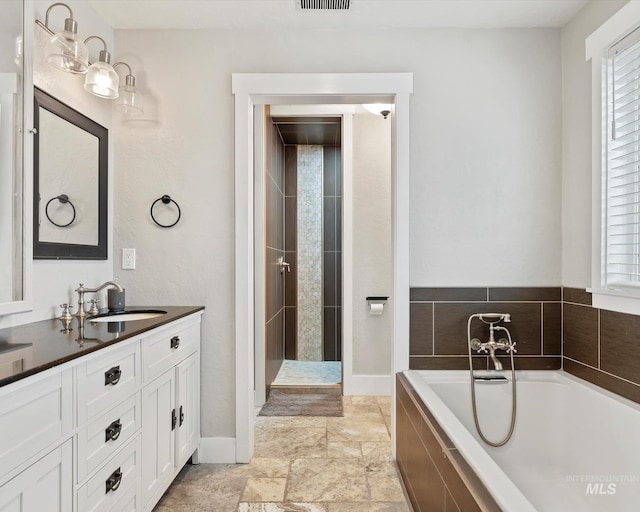 bathroom featuring a relaxing tiled tub and vanity