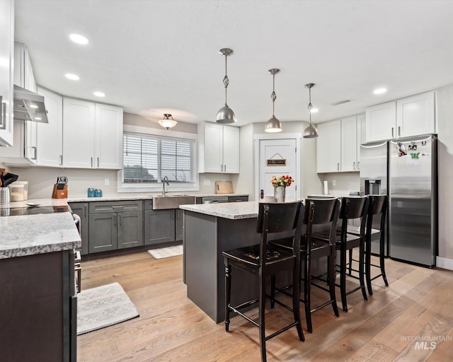 kitchen with stainless steel fridge with ice dispenser, a breakfast bar, a kitchen island, white cabinetry, and decorative light fixtures