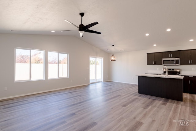 kitchen featuring an island with sink, light countertops, vaulted ceiling, appliances with stainless steel finishes, and open floor plan
