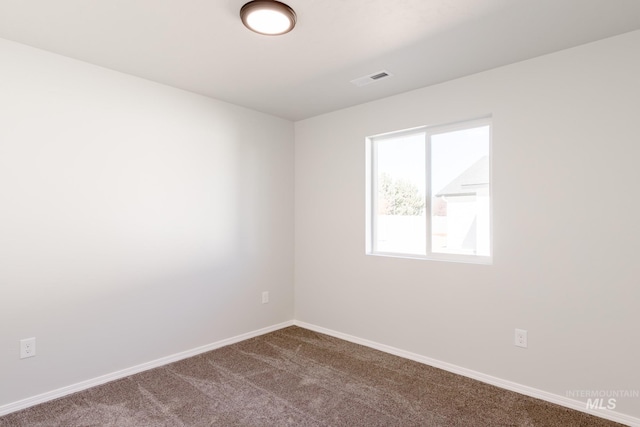 unfurnished room with dark colored carpet, visible vents, and baseboards