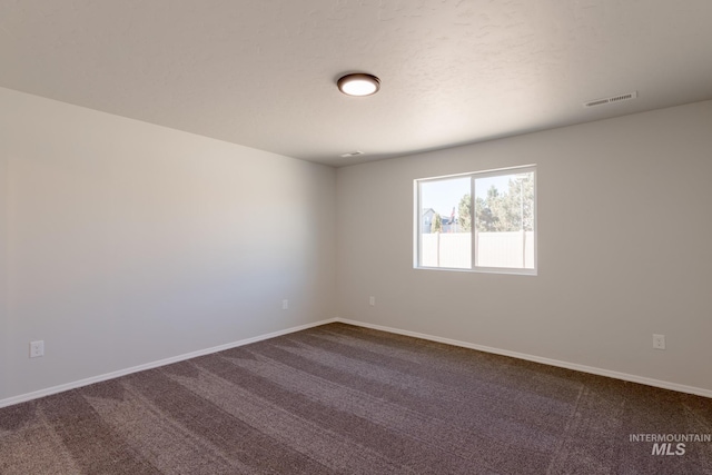 spare room with baseboards, dark colored carpet, and visible vents