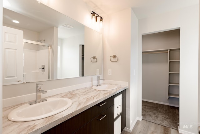 full bath featuring visible vents, a sink, a shower with shower door, and a walk in closet