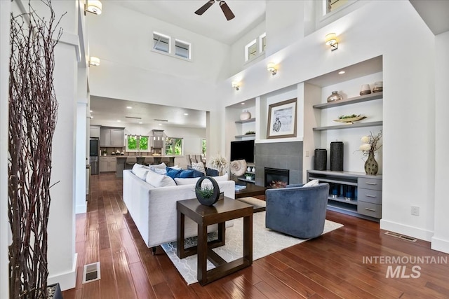 356 E Lake Briar Ln, Eagle, ID 83616 - living area with dark wood-style flooring, a tiled fireplace, a ceiling fan, a high ceiling, and built in shelves