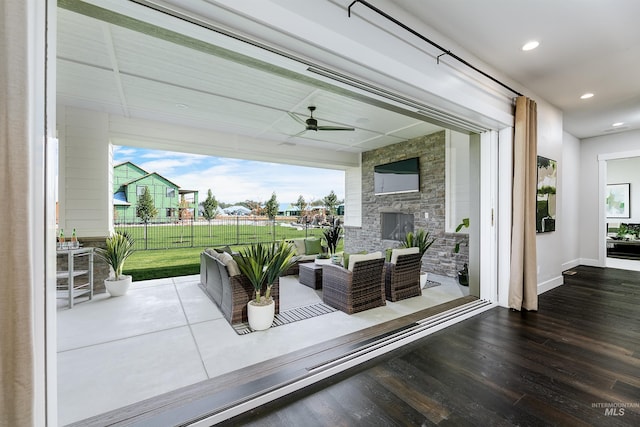 wooden deck featuring ceiling fan, an outdoor living space with a fireplace, and a patio