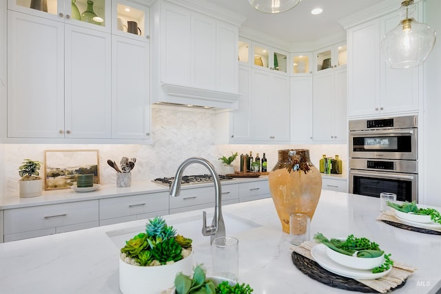kitchen featuring stainless steel appliances, white cabinetry, decorative light fixtures, backsplash, and light stone countertops