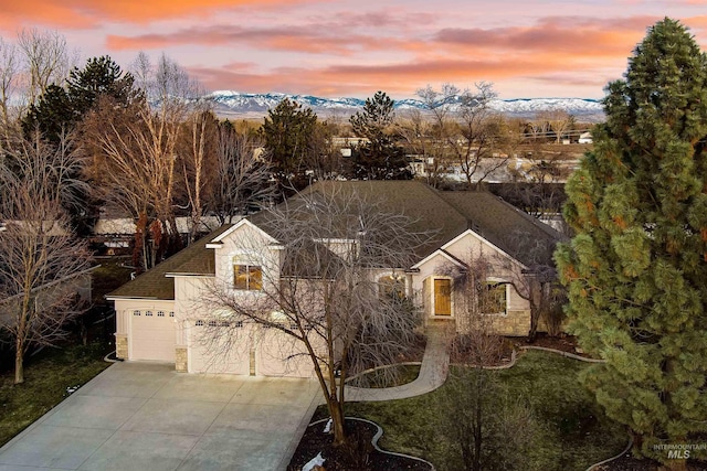 view of front of house featuring roof with shingles, concrete driveway, a mountain view, a garage, and stone siding