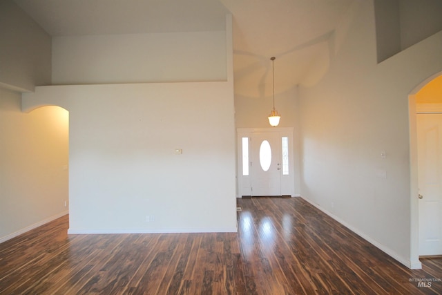 entryway featuring arched walkways, a towering ceiling, dark wood-type flooring, and baseboards