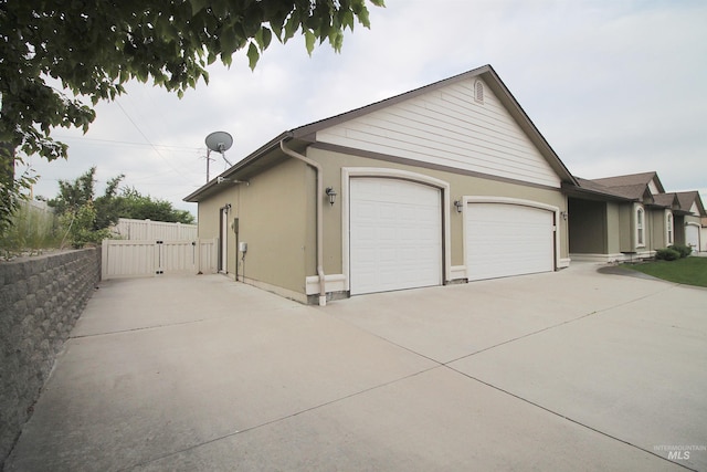 view of side of home with concrete driveway, an attached garage, a gate, and stucco siding