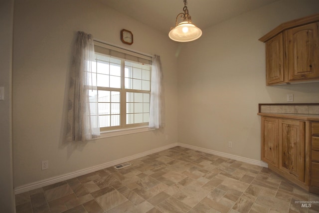 unfurnished dining area with stone finish floors and baseboards