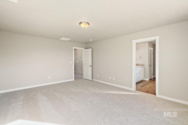 unfurnished bedroom with ensuite bathroom and light carpet