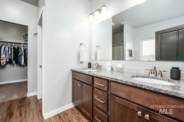 full bath with baseboards, a walk in closet, a sink, and wood finished floors