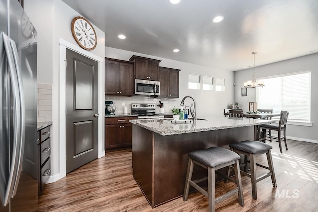 kitchen featuring wood finished floors, a sink, dark brown cabinets, appliances with stainless steel finishes, and a kitchen bar