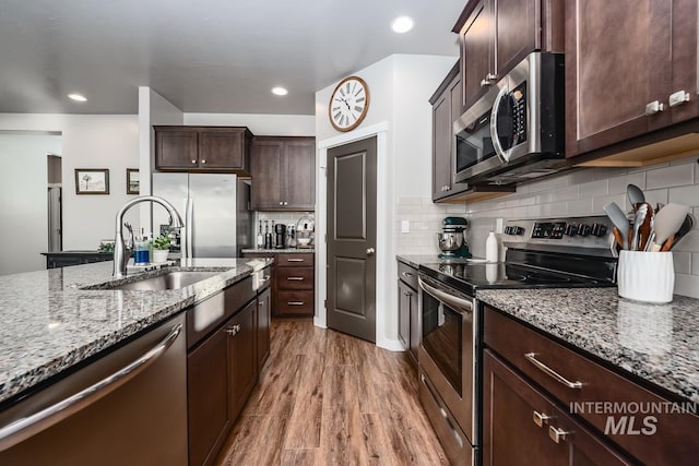 kitchen with light stone countertops, appliances with stainless steel finishes, a sink, dark brown cabinetry, and wood finished floors