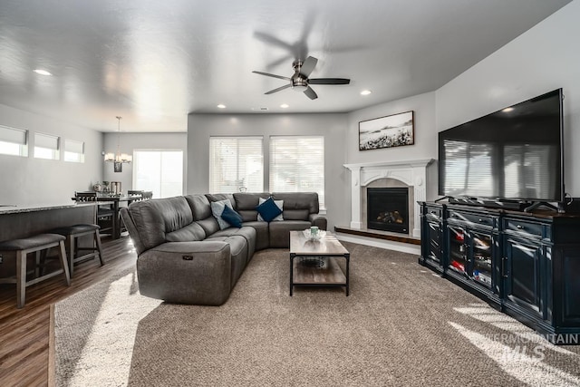 living area with ceiling fan with notable chandelier, recessed lighting, a fireplace with raised hearth, and wood finished floors