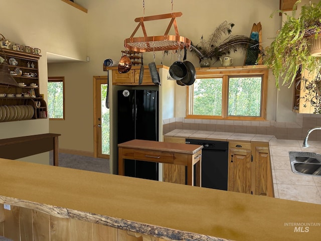 kitchen featuring a healthy amount of sunlight, black dishwasher, sink, and tile countertops