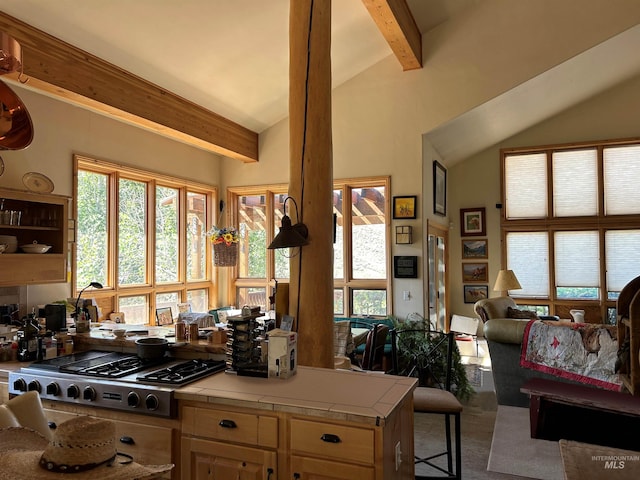 kitchen featuring carpet flooring, beam ceiling, stainless steel gas cooktop, tile counters, and a breakfast bar area