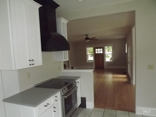 kitchen with wall chimney range hood, light wood-type flooring, ceiling fan, high end range, and kitchen peninsula