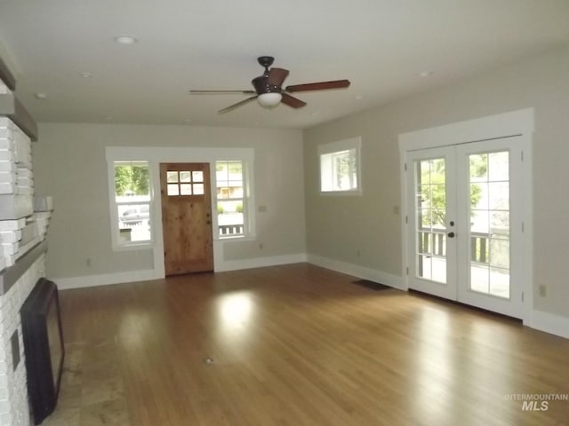 unfurnished living room featuring ceiling fan, a brick fireplace, hardwood / wood-style floors, and french doors