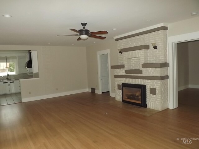 unfurnished living room featuring ceiling fan, a fireplace, sink, and hardwood / wood-style floors