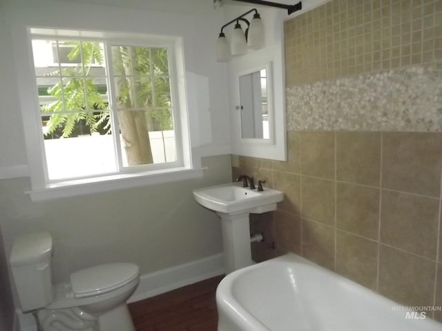 bathroom with toilet, tile walls, and a tub to relax in