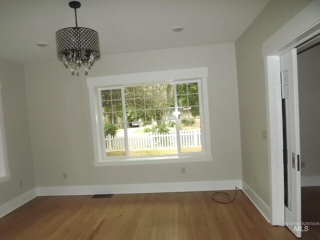 unfurnished room with a notable chandelier, a healthy amount of sunlight, and wood-type flooring