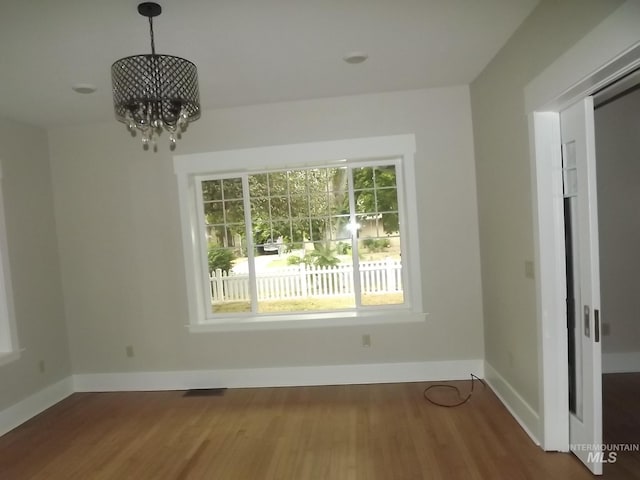 unfurnished dining area with wood-type flooring and a notable chandelier