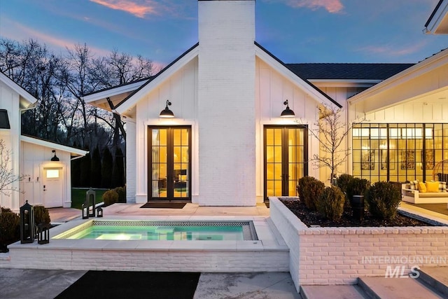 back house at dusk featuring a patio, french doors, and a hot tub