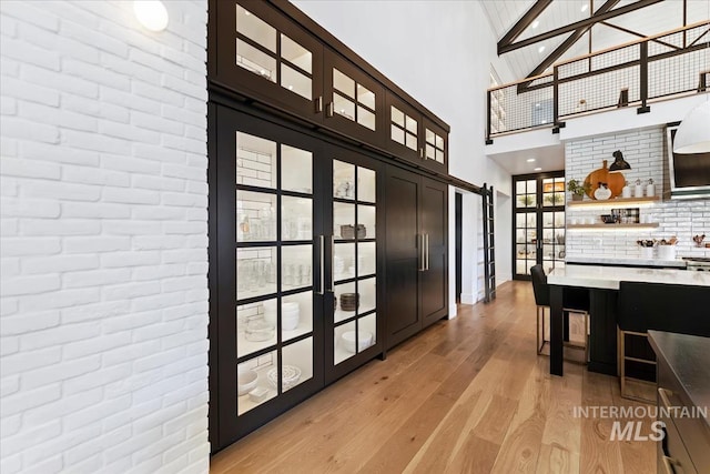 entryway featuring a towering ceiling, light hardwood / wood-style flooring, a barn door, and brick wall