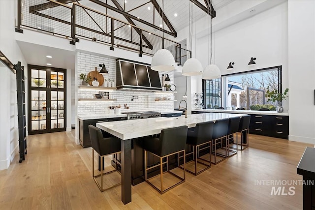 kitchen featuring wall chimney range hood, a breakfast bar, decorative light fixtures, and high vaulted ceiling