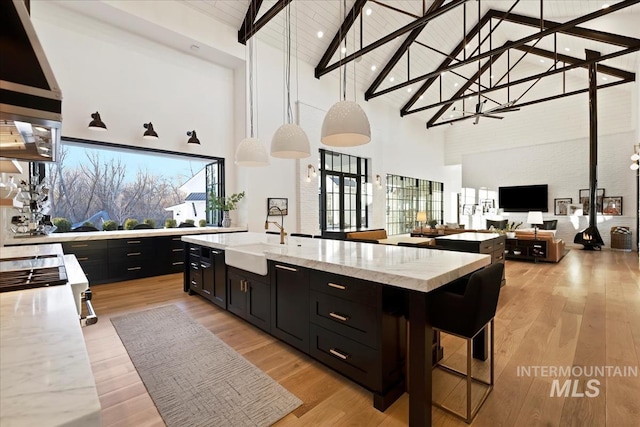 kitchen with beam ceiling, sink, light stone counters, high vaulted ceiling, and a breakfast bar