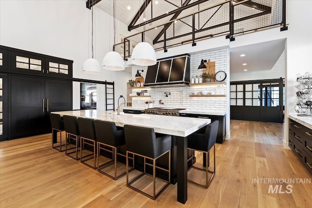 kitchen with exhaust hood, a barn door, high vaulted ceiling, light wood-type flooring, and pendant lighting