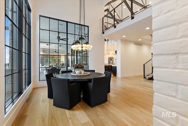 dining area with light hardwood / wood-style floors, a healthy amount of sunlight, a towering ceiling, and an inviting chandelier