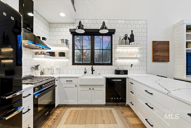 kitchen with white cabinets, backsplash, light stone countertops, light wood-type flooring, and black appliances