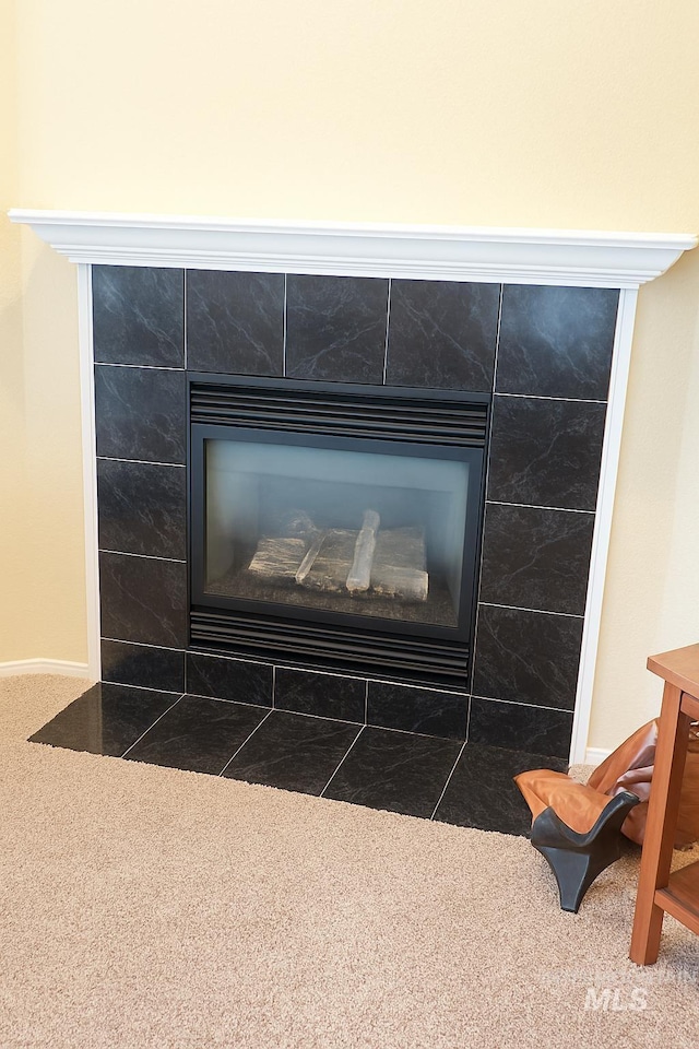 details featuring a tiled fireplace, carpet, and baseboards