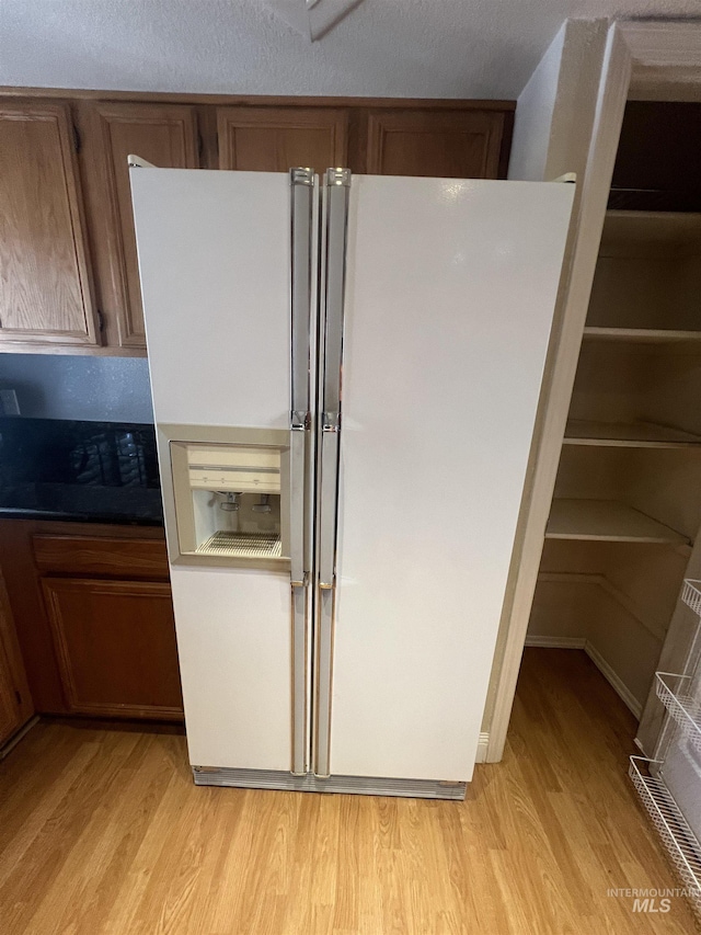 kitchen featuring brown cabinets, white fridge with ice dispenser, and light wood-style floors