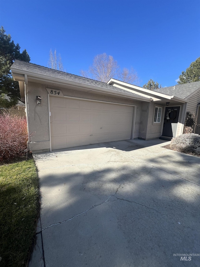 exterior space featuring a garage, stucco siding, concrete driveway, and roof with shingles