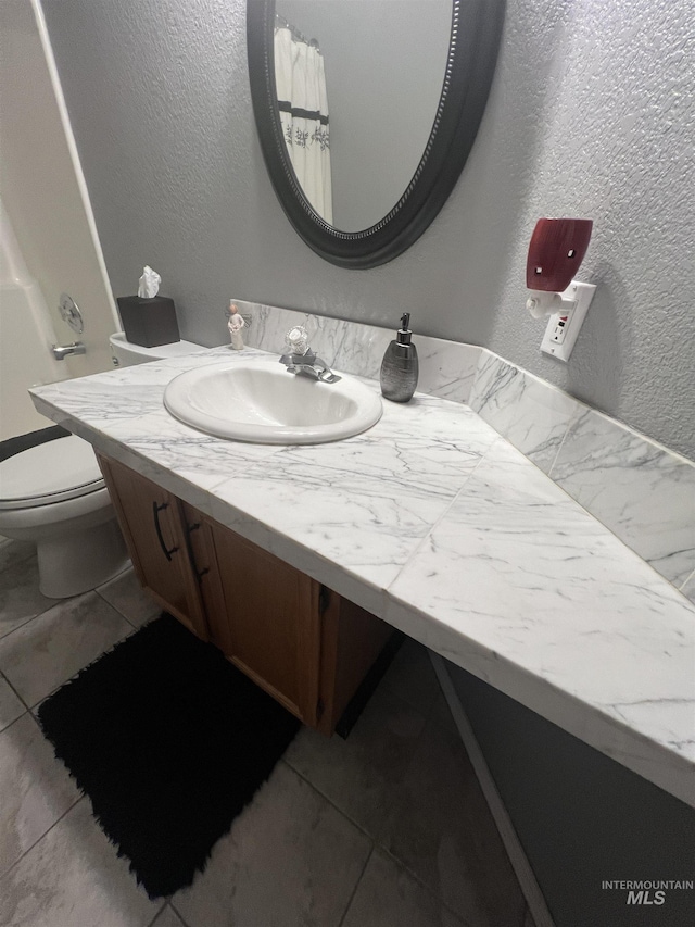 bathroom featuring vanity, a textured wall, and toilet