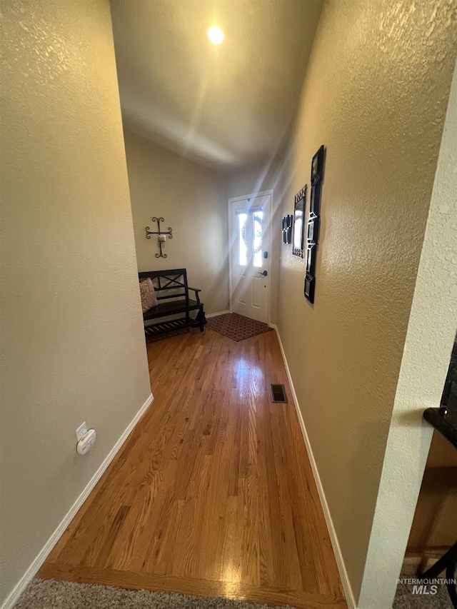 hallway featuring baseboards, visible vents, a textured wall, and wood finished floors